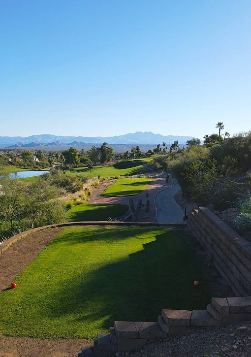 Elevated tee looking down a green fairway with saguaro cactus, a lake and desert mountains at Desert Canyon Golf Club in Fountain Hills, Arizona